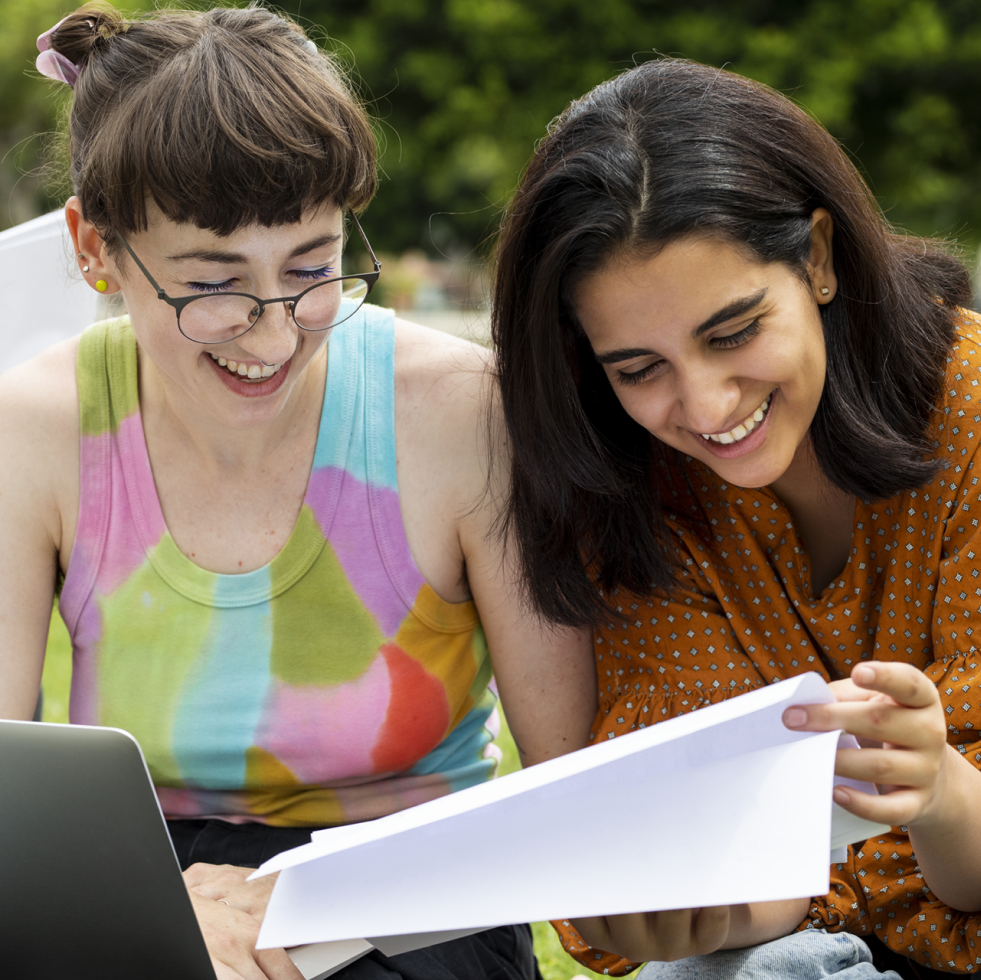 Due persone sorridenti della Fondazione Capacci stanno leggendo dei documenti all'aperto, con un computer portatile sul tavolo.